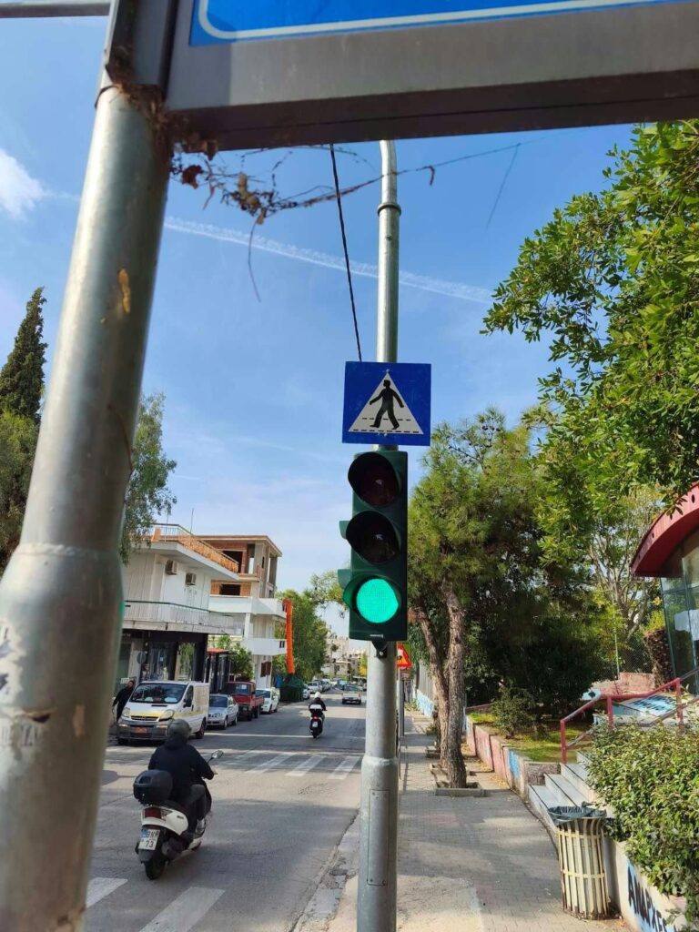 Νέος φωτεινός σηματοδότης στην οδό Αρχιεπισκόπου Χρυσοστόμου Αθηνών στον Βύρωνα 3 Φωτεινός σηματοδότης με πινακίδα διάβασης πεζών σε δρόμο του Βύρωνα, με μοτοσικλέτα και αυτοκίνητα στο βάθος