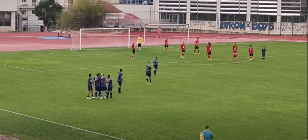 Πέντε στα πέντε η Δόξα Βύρωνος, 2-0 την Αμφιάλη 1 Ποδοσφαιριστές με μπλε φανέλες πανηγυρίζουν αγκαλιασμένοι στο γήπεδο, ενώ παίκτες με κόκκινες φανέλες επιστρέφουν προς το κέντρο.